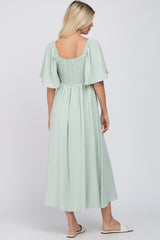 woman wearing a mint green midi dress with flutter sleeves and a smocked back detail