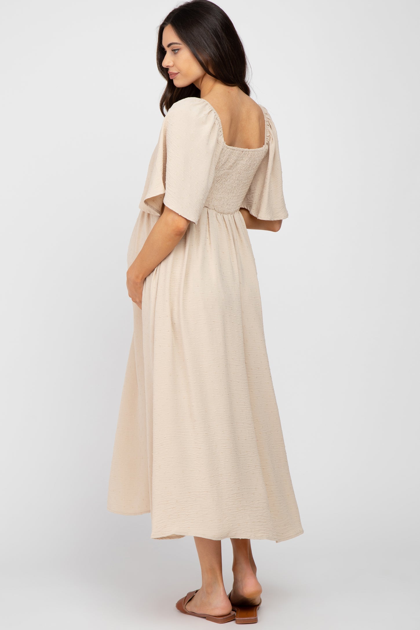 woman wearing a beige maternity maxi dress with a square neckline and puff sleeves, showing her baby bump