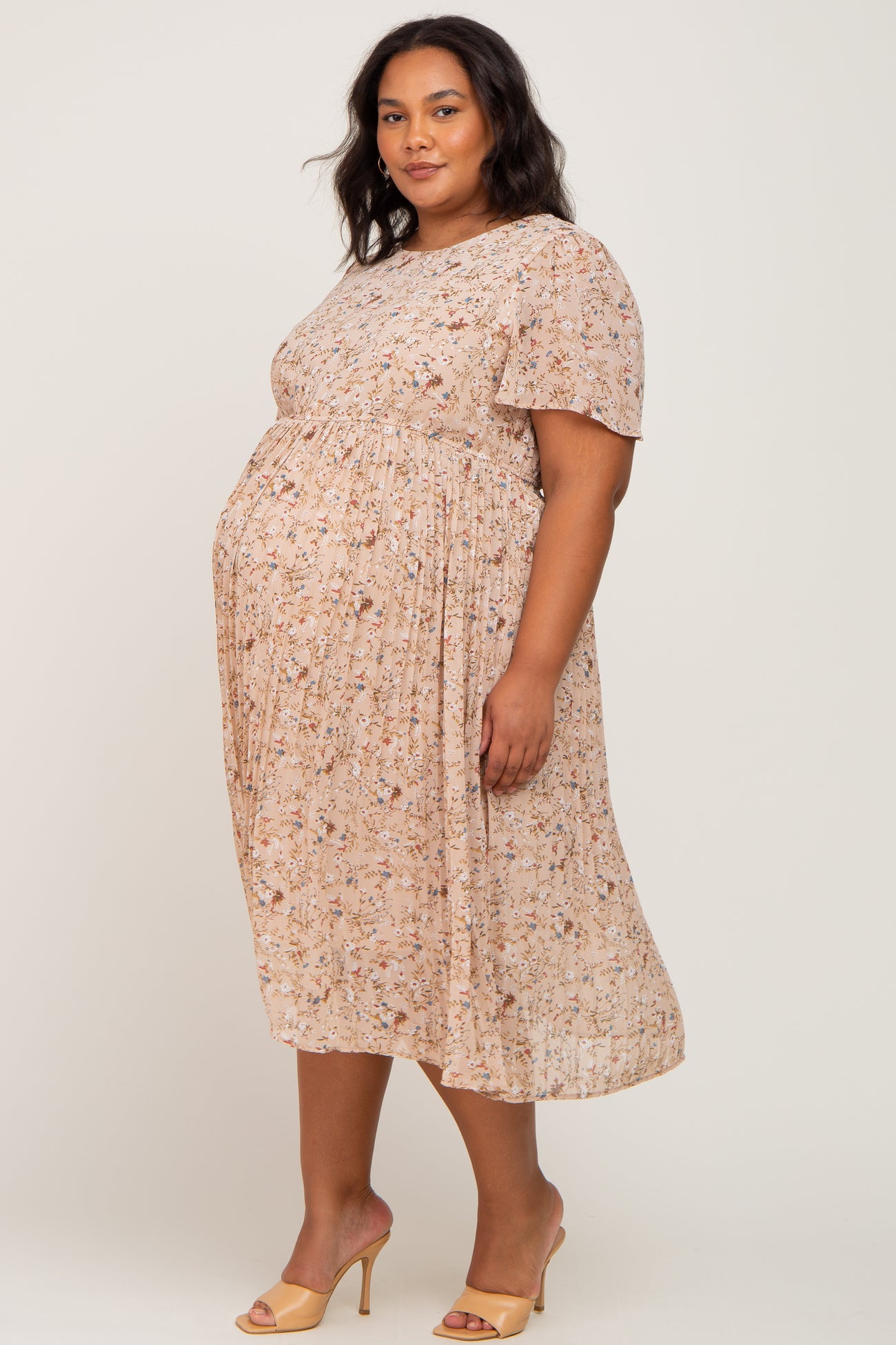 woman wearing a floral short sleeve maternity dress with a visible baby bump, standing in a relaxed pose