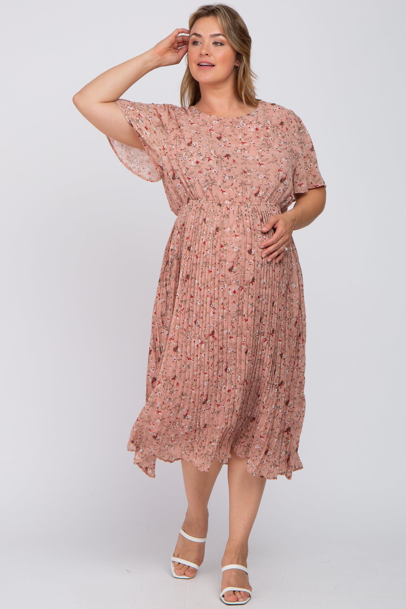woman wearing a blush pink floral maternity dress with a pleated skirt and short sleeves, gently cradling her baby bump