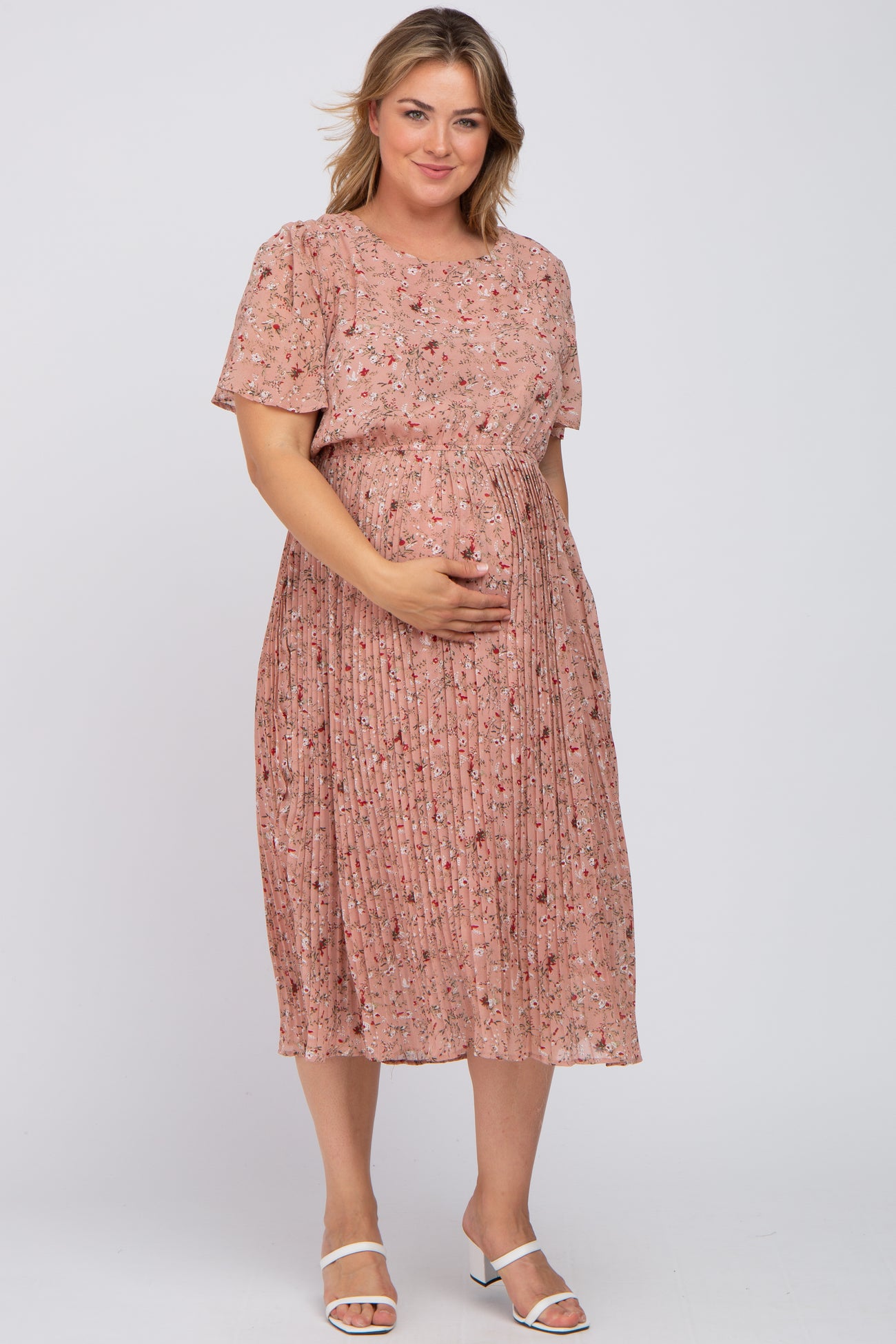 woman wearing a pink floral pleated maternity dress and gently cradling her baby bump