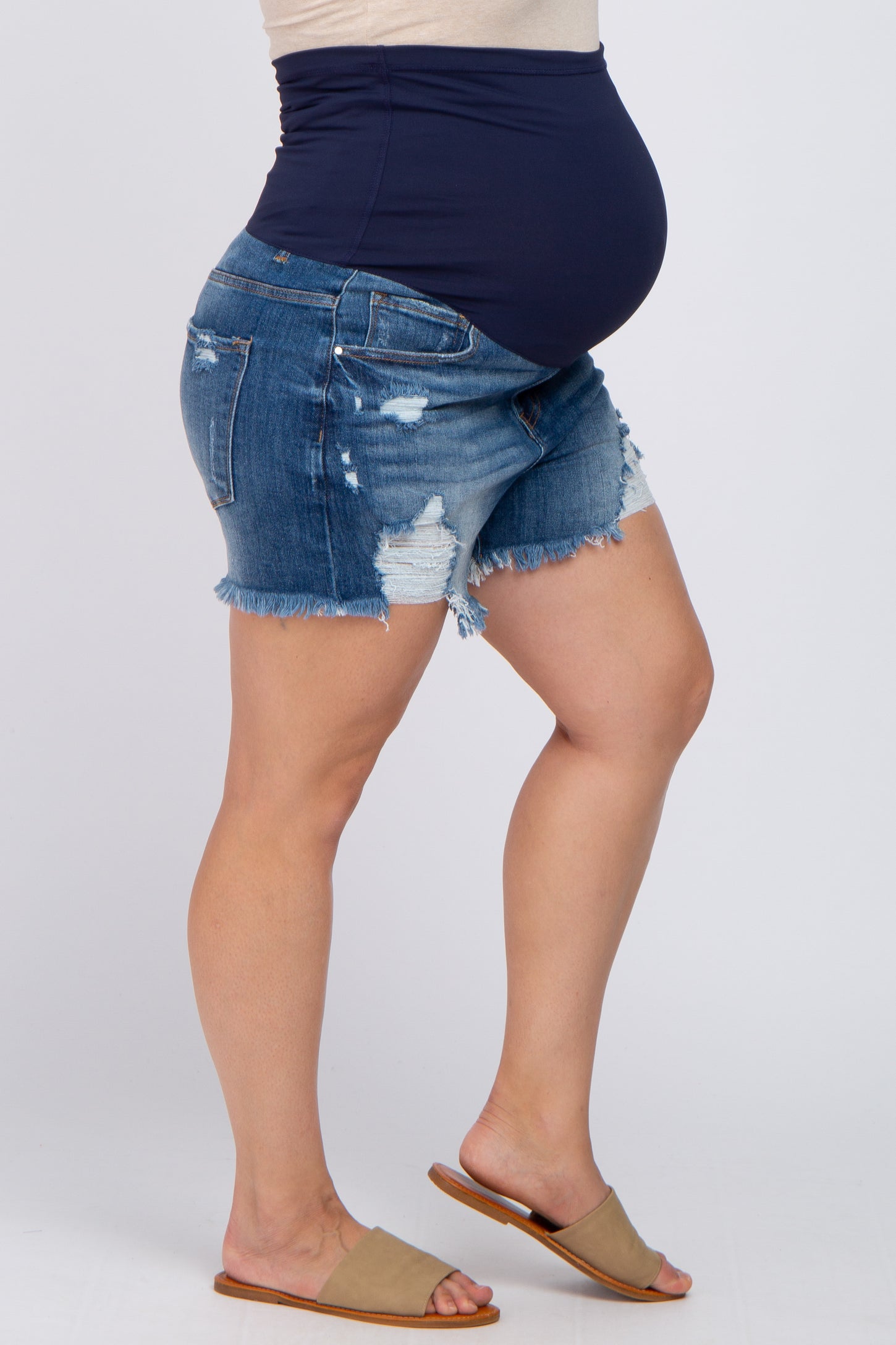 Pregnant woman wearing distressed denim maternity shorts with a navy blue over-the-belly support band