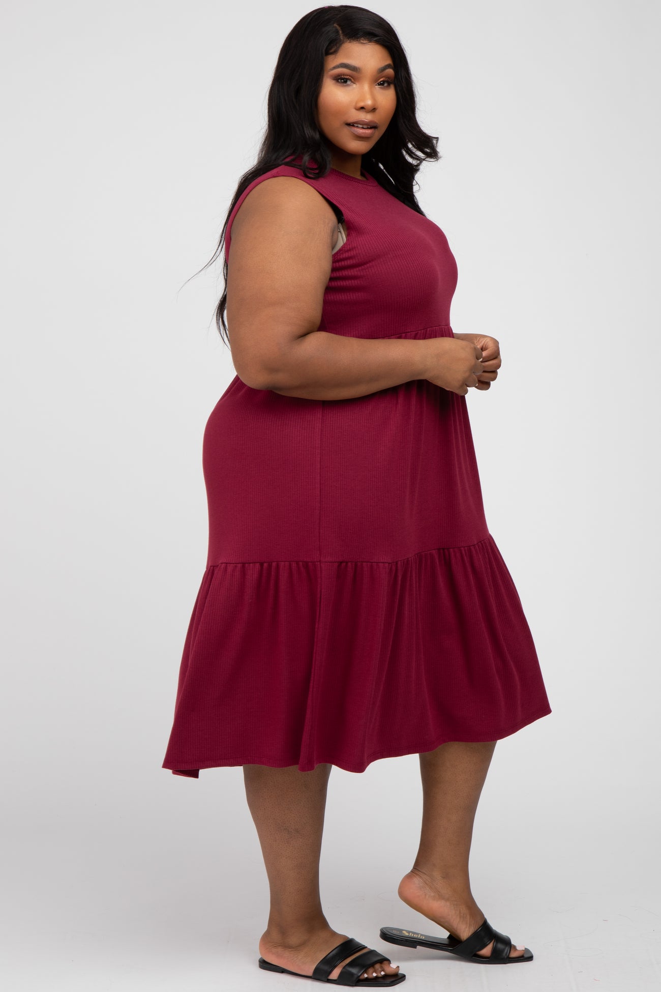 Plus size woman wearing a sleeveless burgundy ribbed tiered midi dress and black sandals