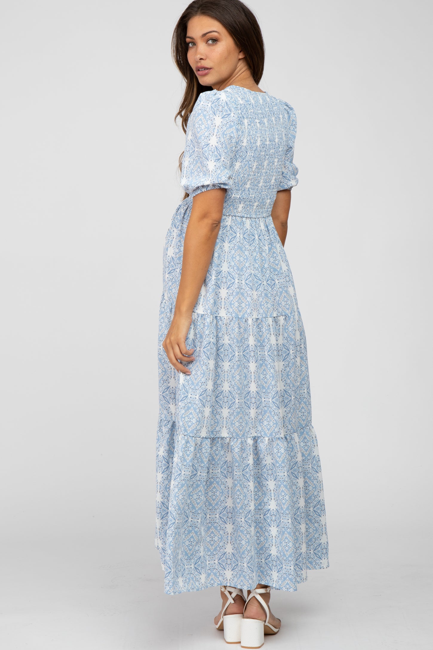 woman wearing a light blue floral maternity maxi dress with short sleeves and a tiered skirt, showing her baby bump