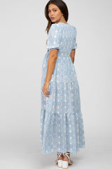 woman wearing a light blue floral maternity maxi dress with short sleeves and a tiered skirt, showing her baby bump