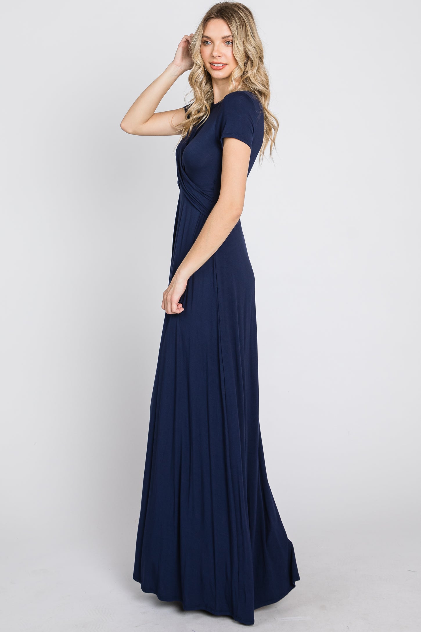 Woman with blonde hair wearing a short sleeve navy blue maxi dress with a wrap bodice against a white background