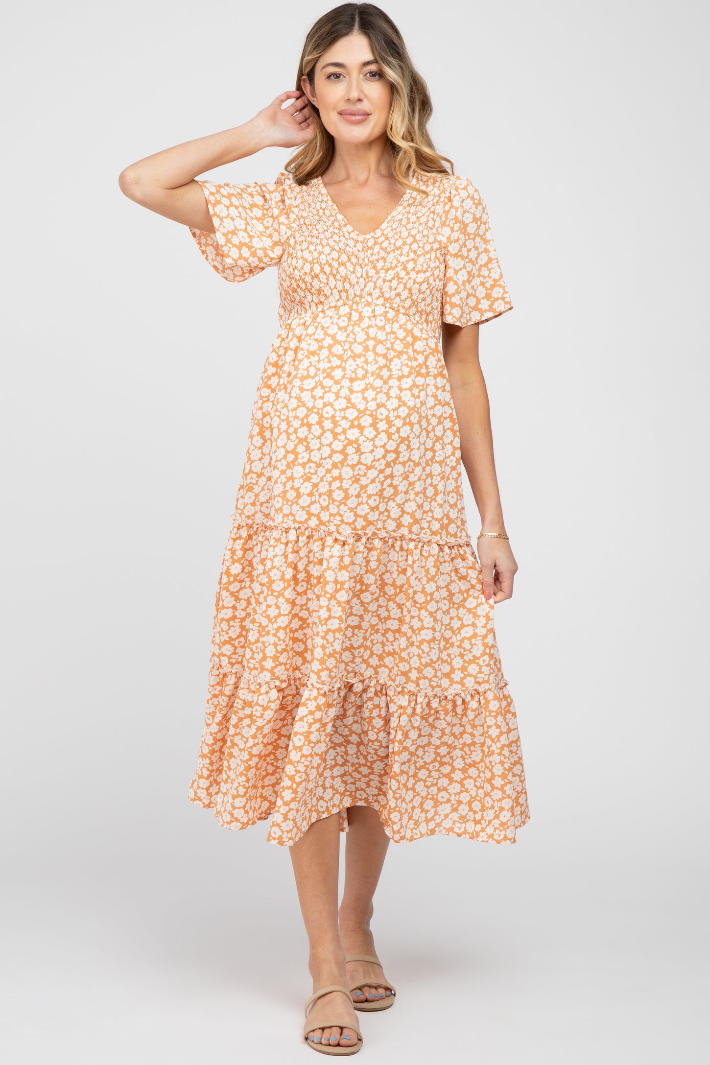woman wearing a short sleeve orange floral maternity dress with a tiered skirt and a baby bump visible