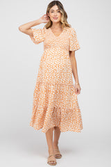 woman wearing a short sleeve orange floral maternity dress with a tiered skirt and a baby bump visible