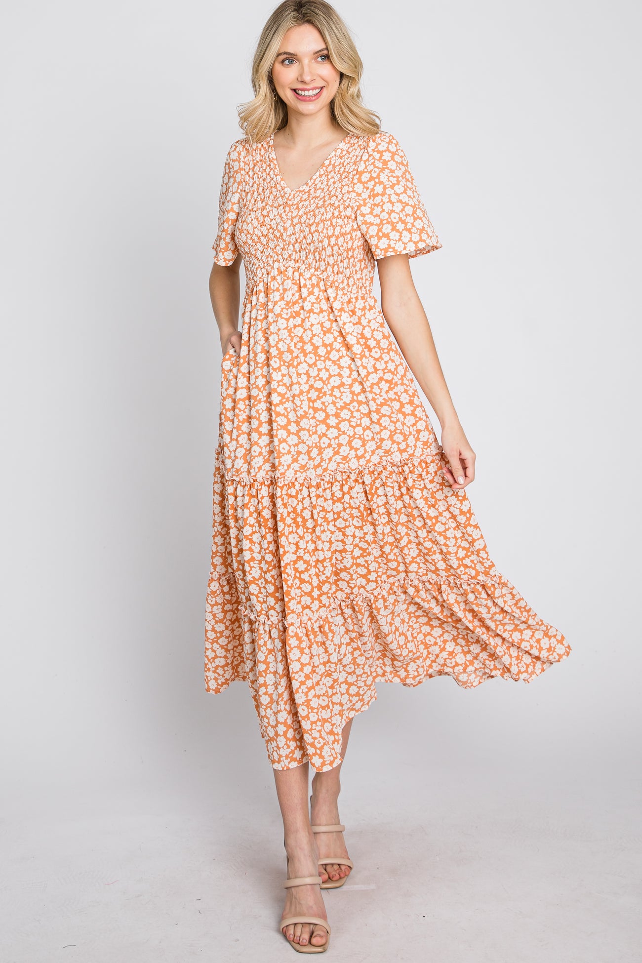 woman wearing a short sleeve orange floral maxi dress with a v-neck and tiered skirt, smiling at the camera