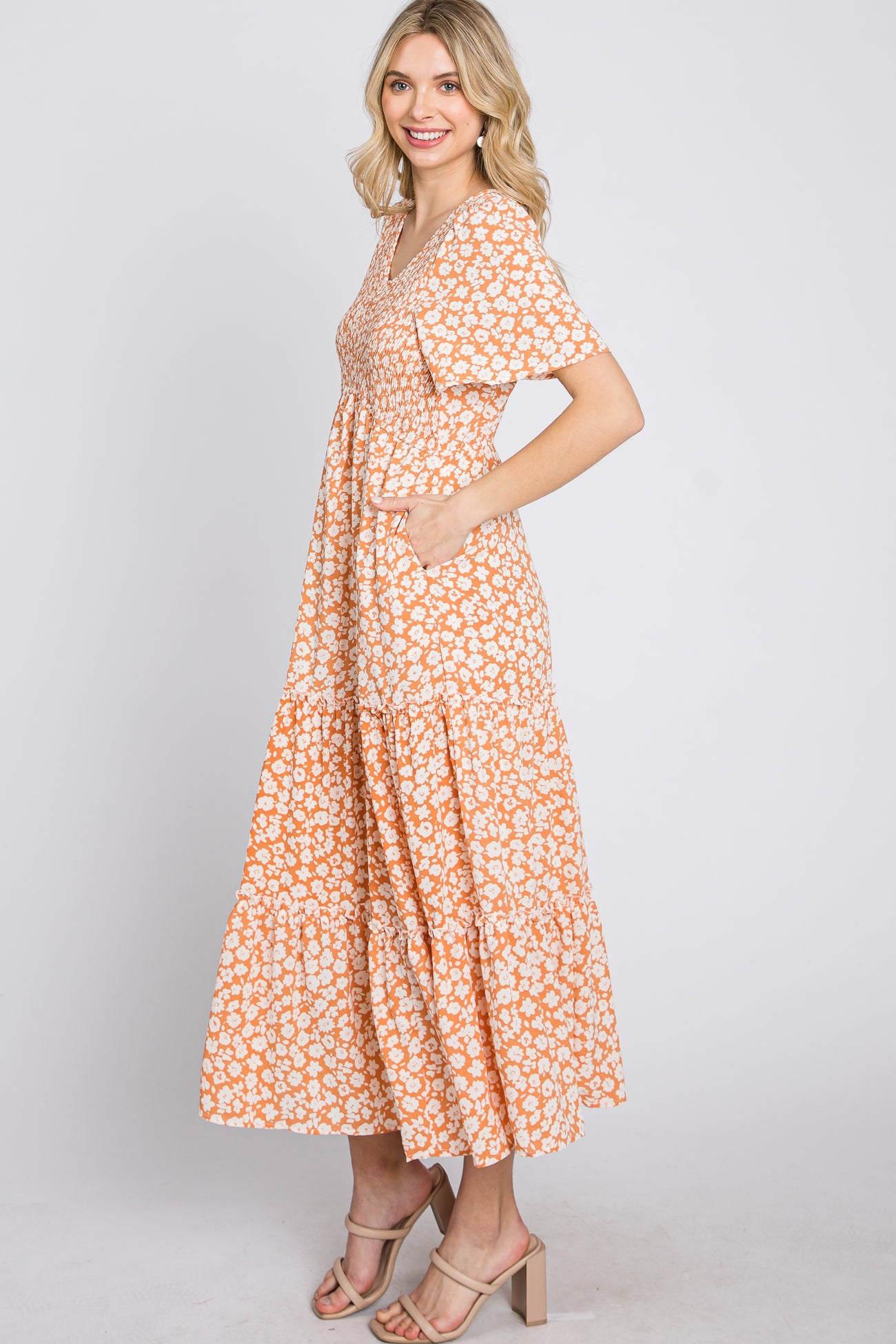 woman wearing a floral orange maxi dress with short sleeves and pockets, standing in profile