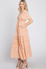 woman wearing a floral orange maxi dress with short sleeves and pockets, standing in profile