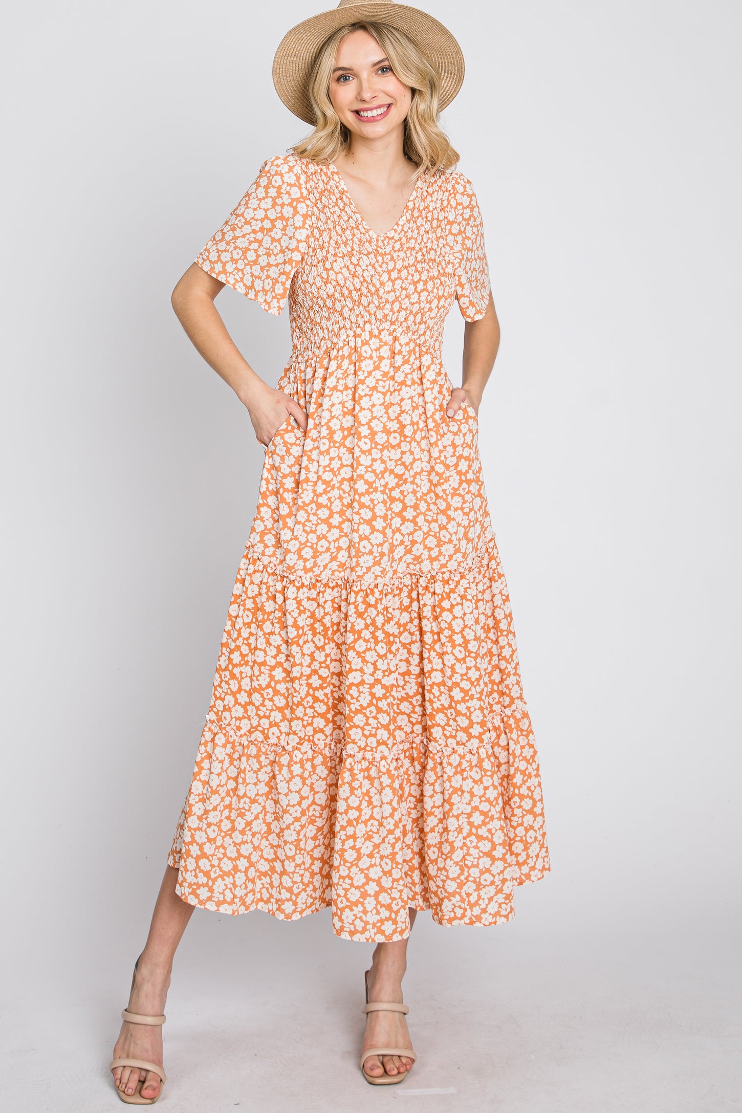woman wearing an orange floral maxi dress with short sleeves and pockets, styled with a straw hat