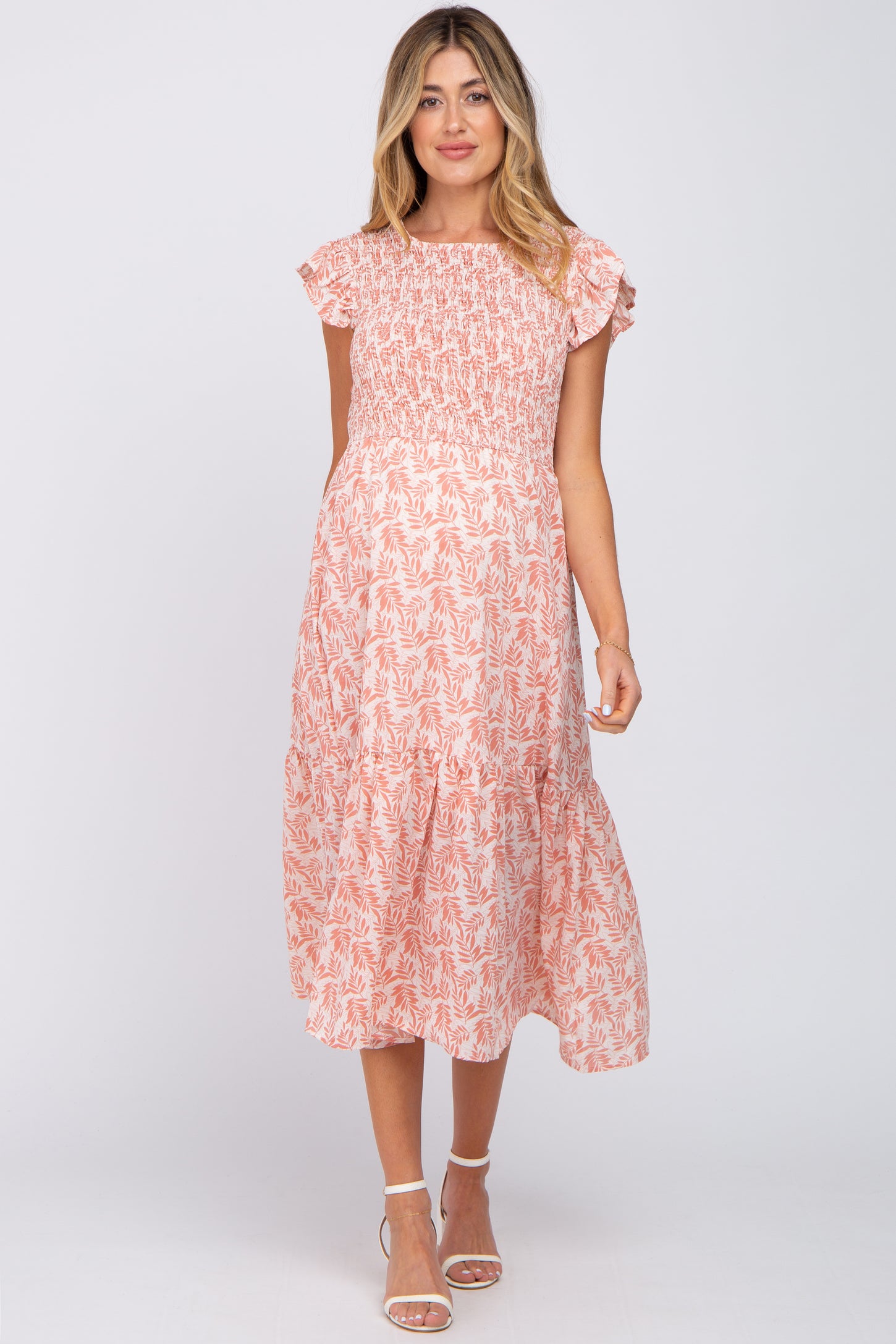 woman wearing a pink patterned maternity dress with short sleeves and a smocked bodice, showing a baby bump