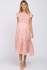 woman wearing a pink patterned maternity dress with short sleeves and a smocked bodice, showing a baby bump