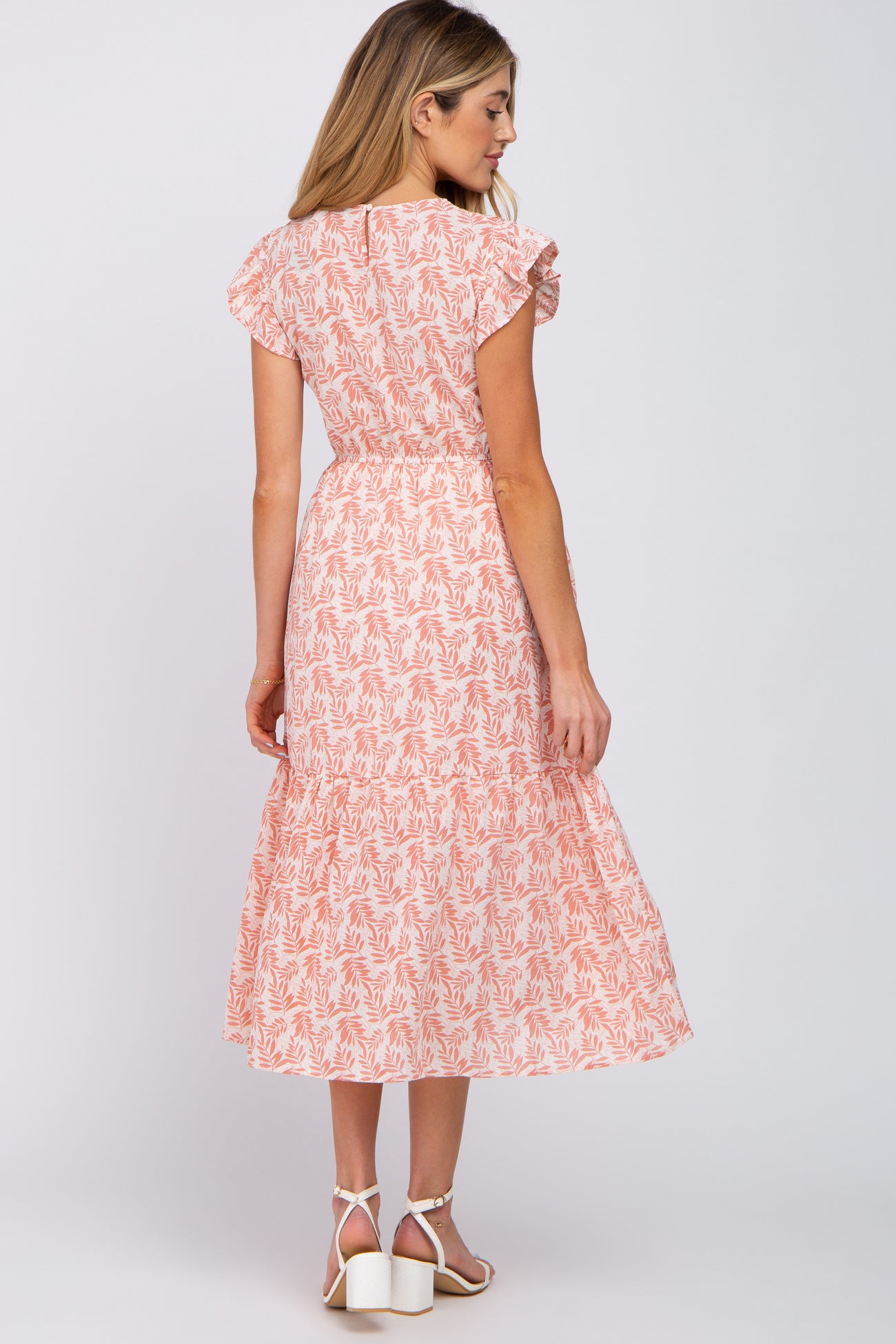 woman wearing a pink patterned maternity dress with flutter sleeves and a tiered skirt, showing a baby bump