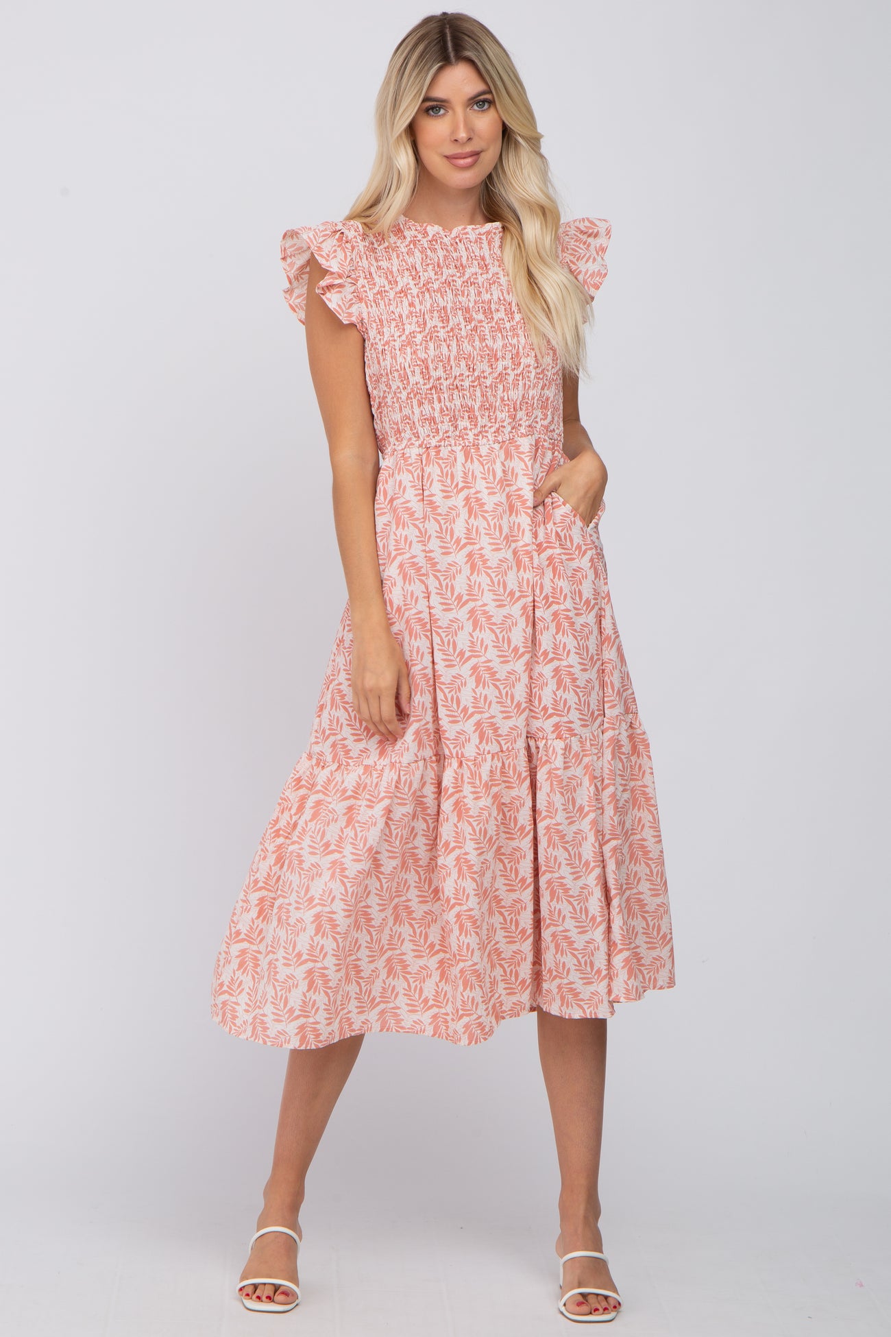 woman wearing a pink floral smocked midi dress with ruffle sleeves and pockets