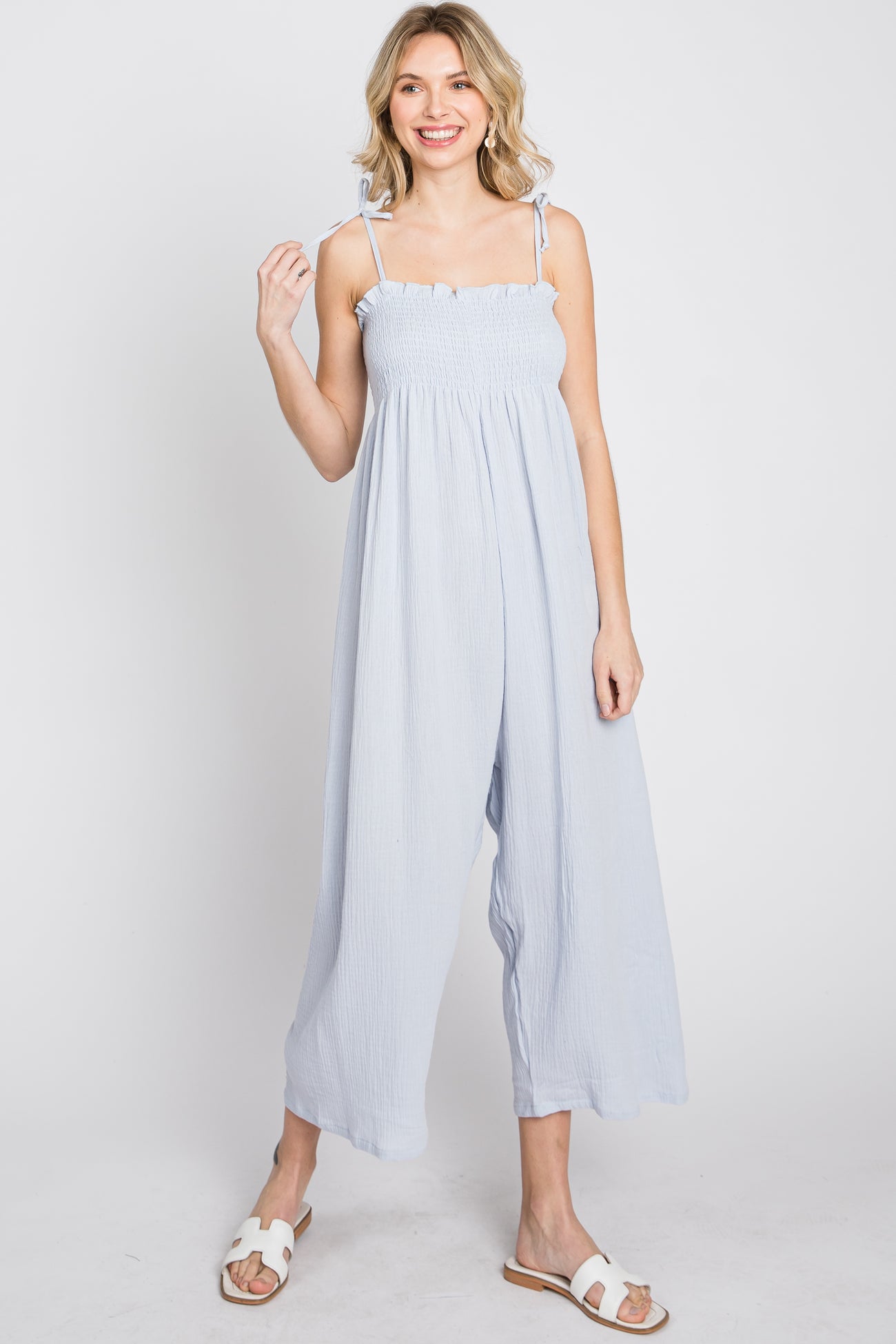 woman wearing light blue smocked wide leg jumpsuit with tie straps and white sandals