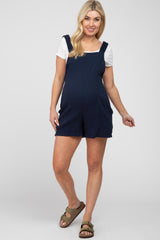 woman wearing a navy maternity romper with straps over a white short sleeve top and showing her baby bump