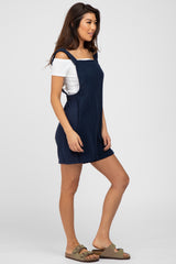 woman wearing navy blue gauze romper over a white off-the-shoulder top and olive green sandals