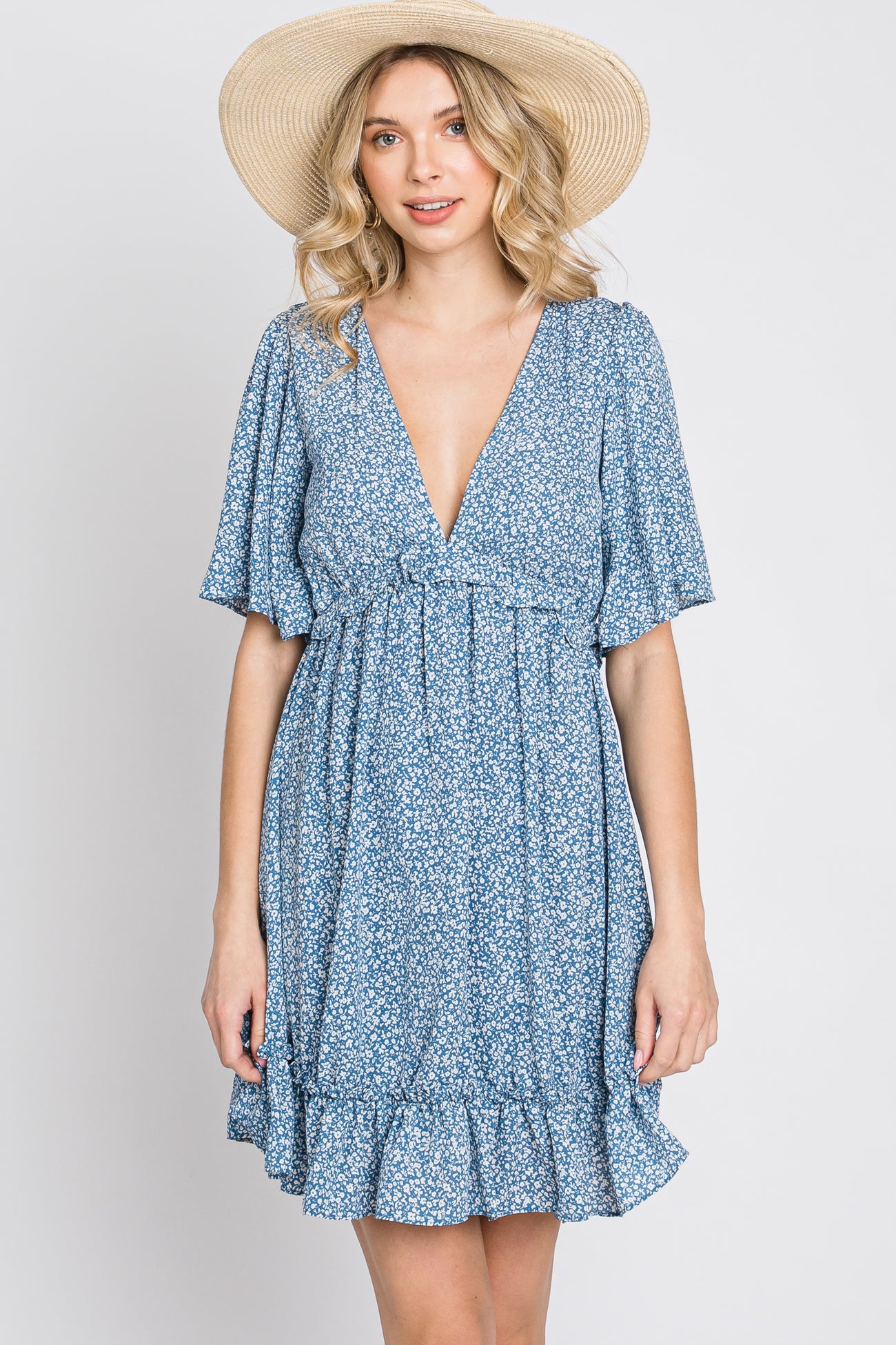 woman wearing a blue floral print mini dress with a v-neckline and a straw sun hat