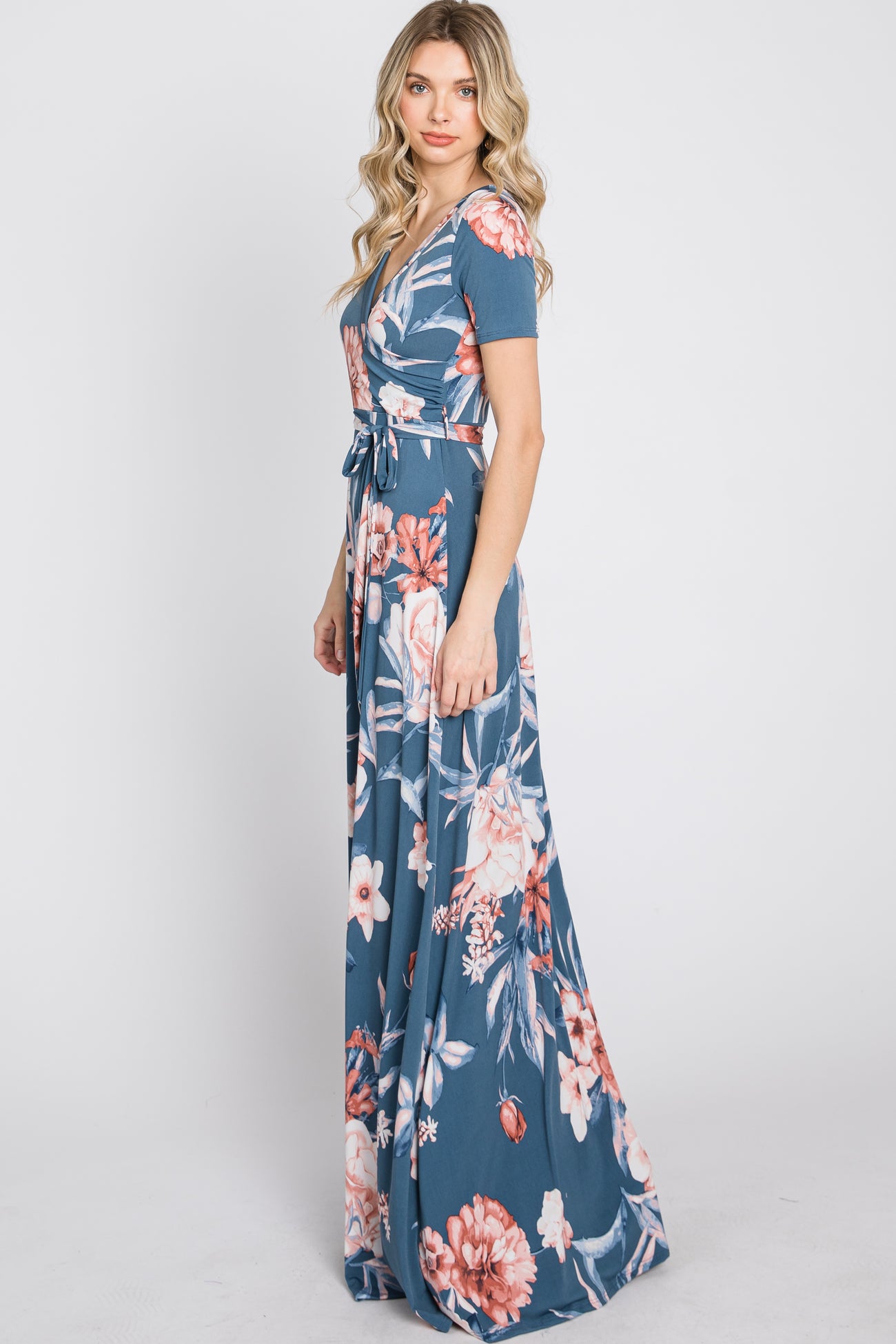 Woman wearing a blue floral maxi wrap dress with short sleeves and a waist tie on a white background