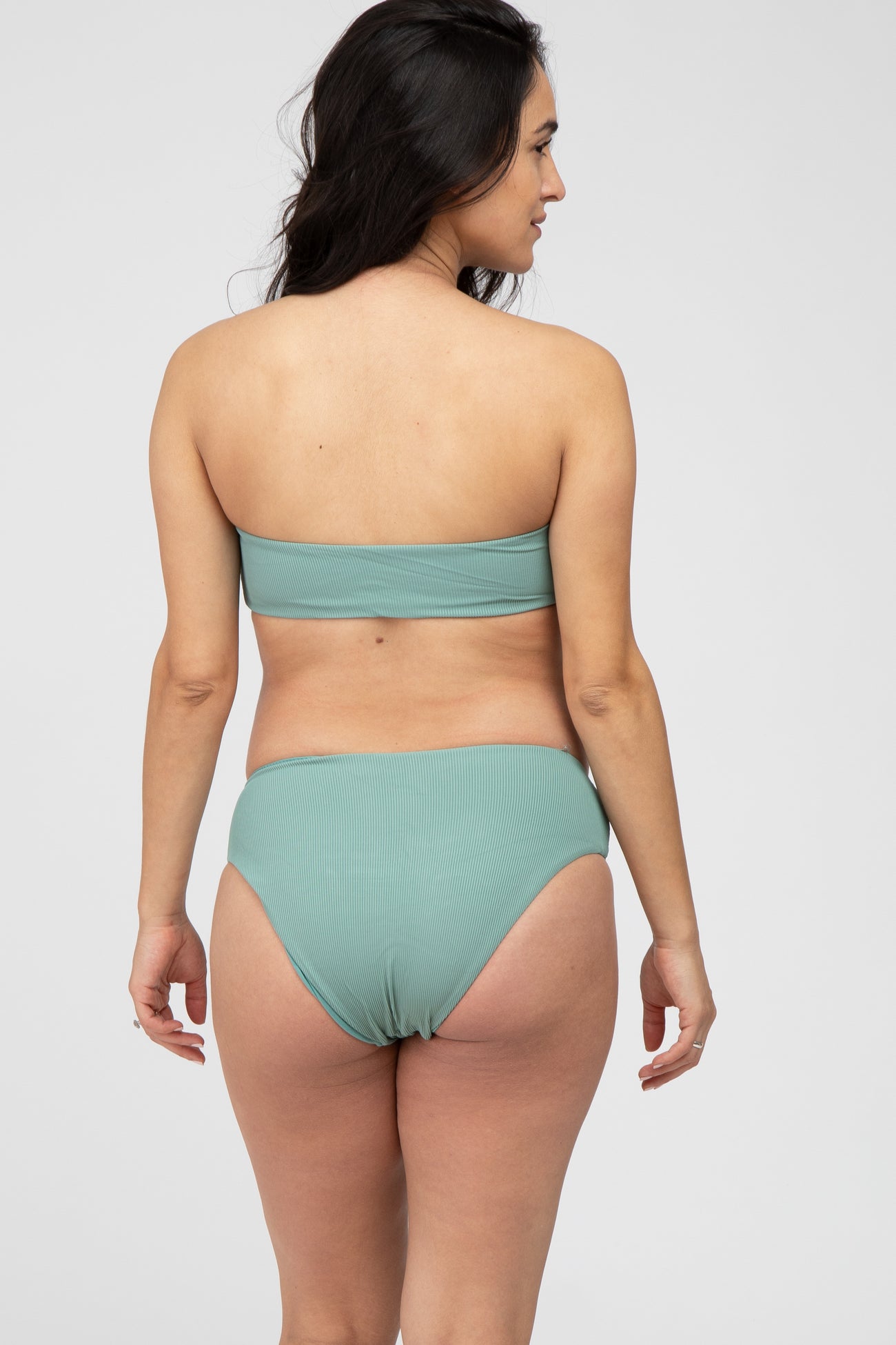 woman wearing a light green ribbed maternity bikini set with a bandeau top and high-waisted bottom