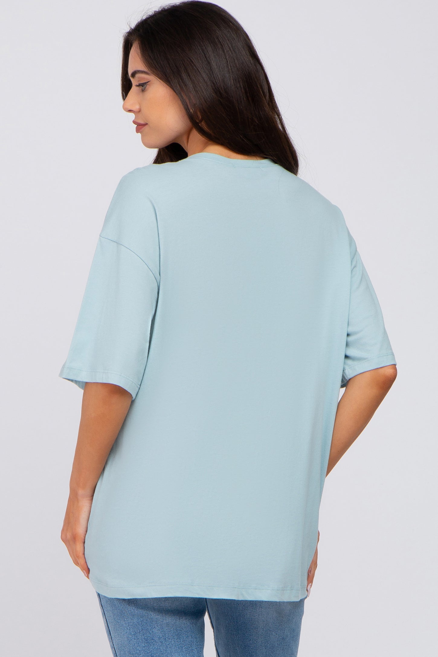 Back view of a woman wearing an oversized light blue t-shirt and denim jeans against a white background