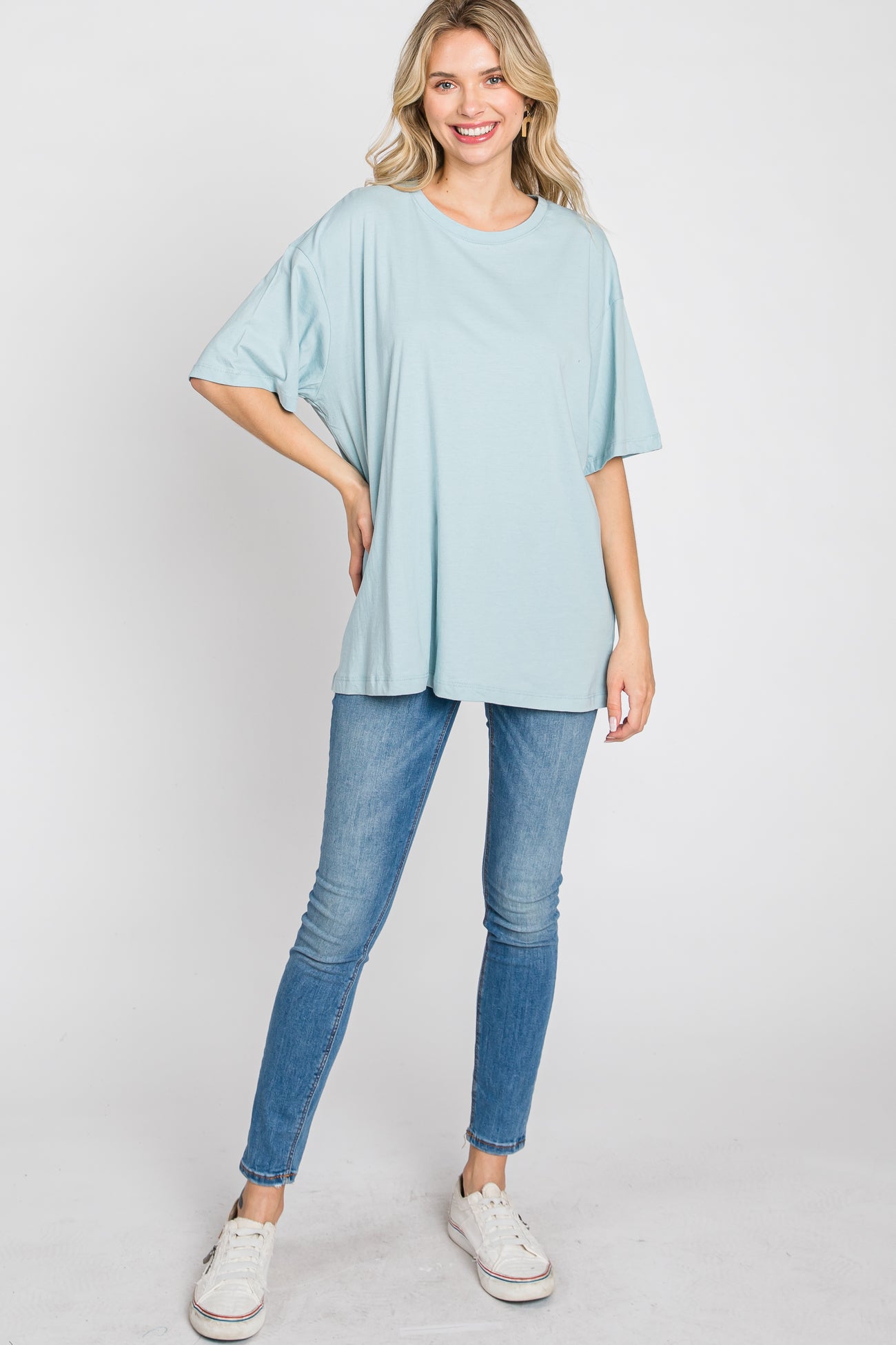 woman wearing a light blue oversized t-shirt and skinny jeans, standing confidently with a smile