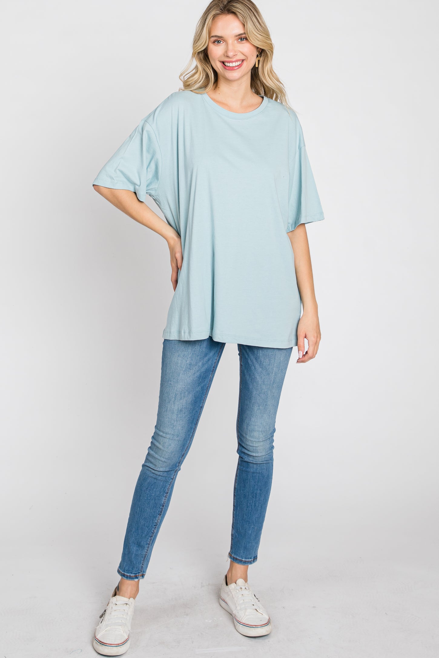 woman wearing a light blue oversized t-shirt and skinny jeans, standing confidently with a smile