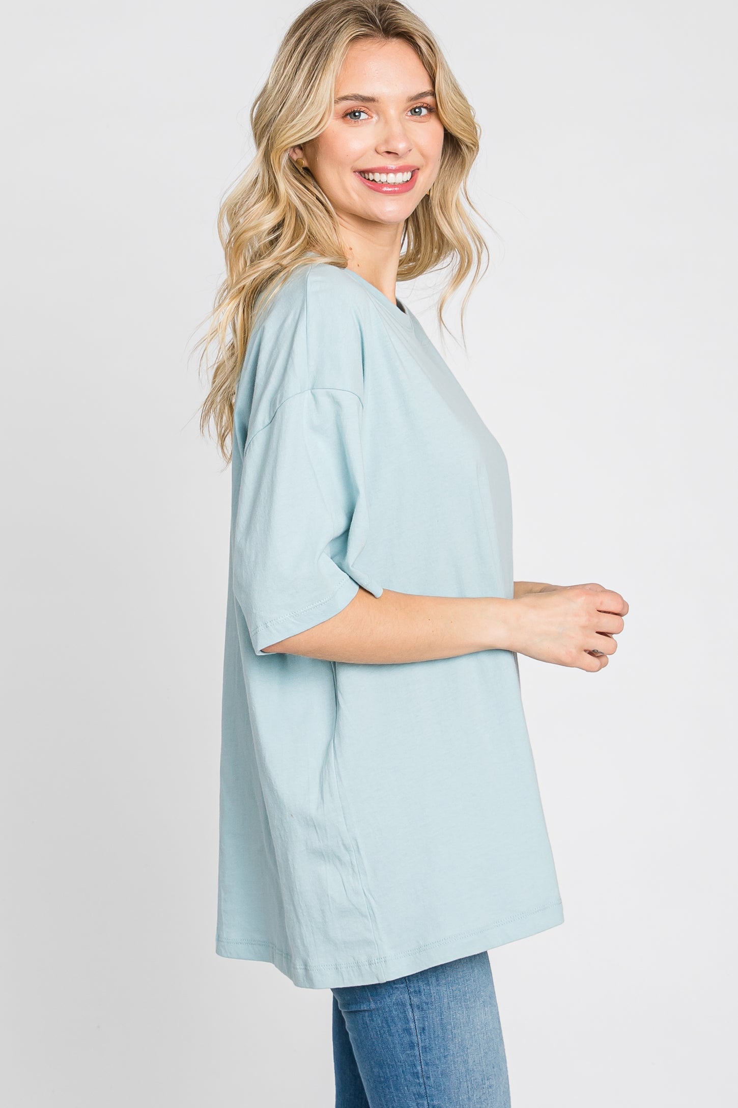 woman wearing a light blue oversized t-shirt with short sleeves and smiling against a neutral background