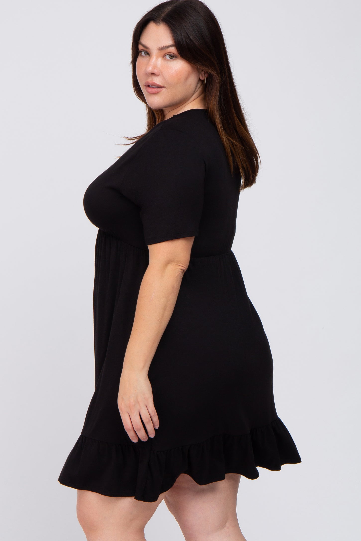 woman wearing a short sleeve black maternity dress with a ruffled hem against a white background