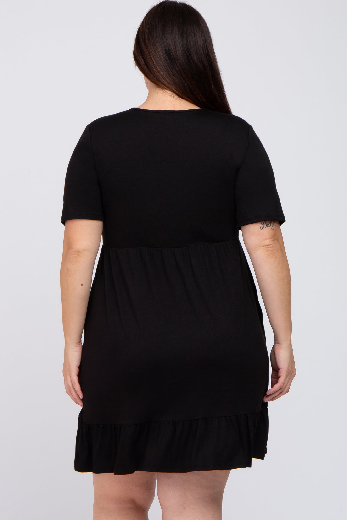 woman wearing a black short sleeve plus size dress with a tiered ruffle hem, seen from the back