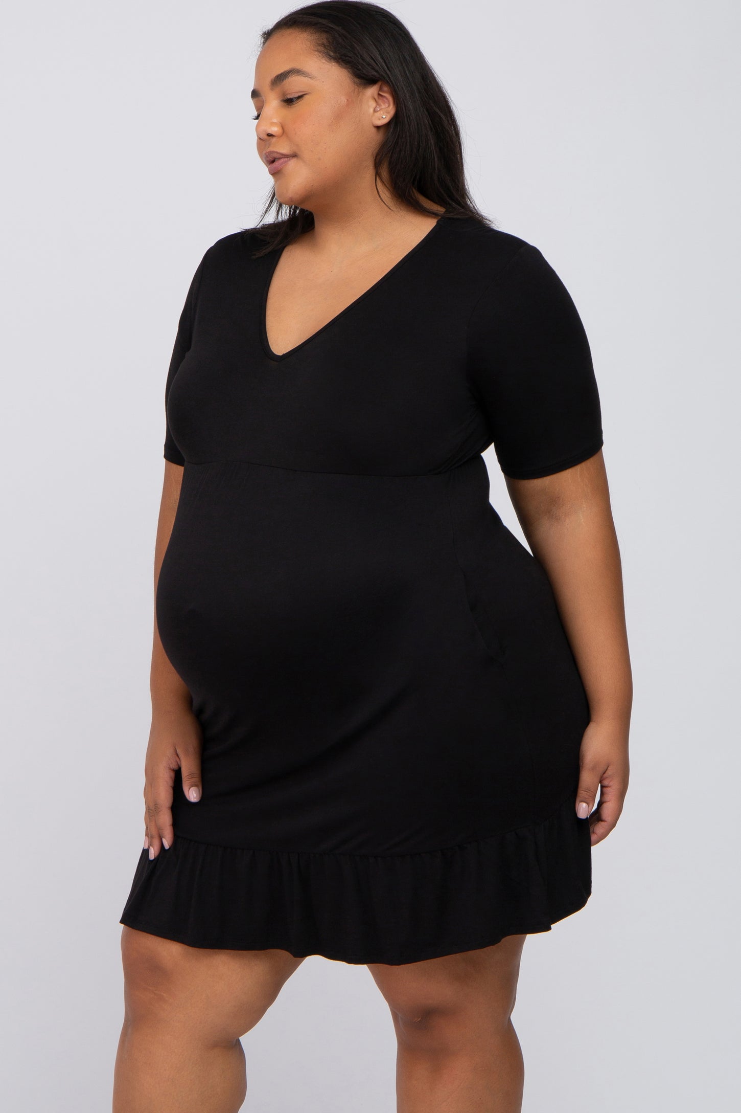 woman wearing a black short sleeve maternity dress with a v-neckline and ruffled hem, showing her baby bump