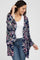 woman wearing a navy floral kimono cardigan over a white top and blue jeans, smiling and posing with one hand raised
