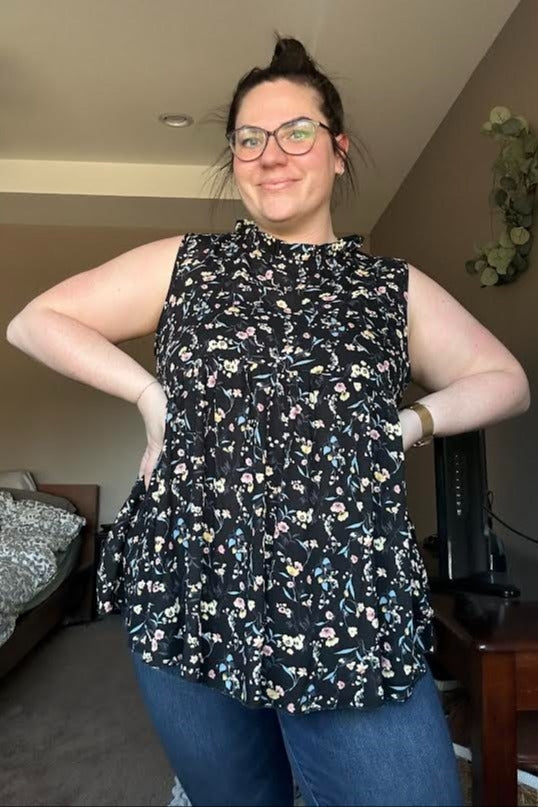 woman wearing a black sleeveless floral print blouse with a high ruffled neckline and blue jeans