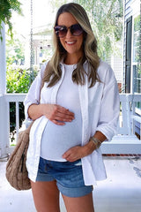 woman wearing a white button-up shirt over a fitted white tank top and denim shorts, showing her baby bump