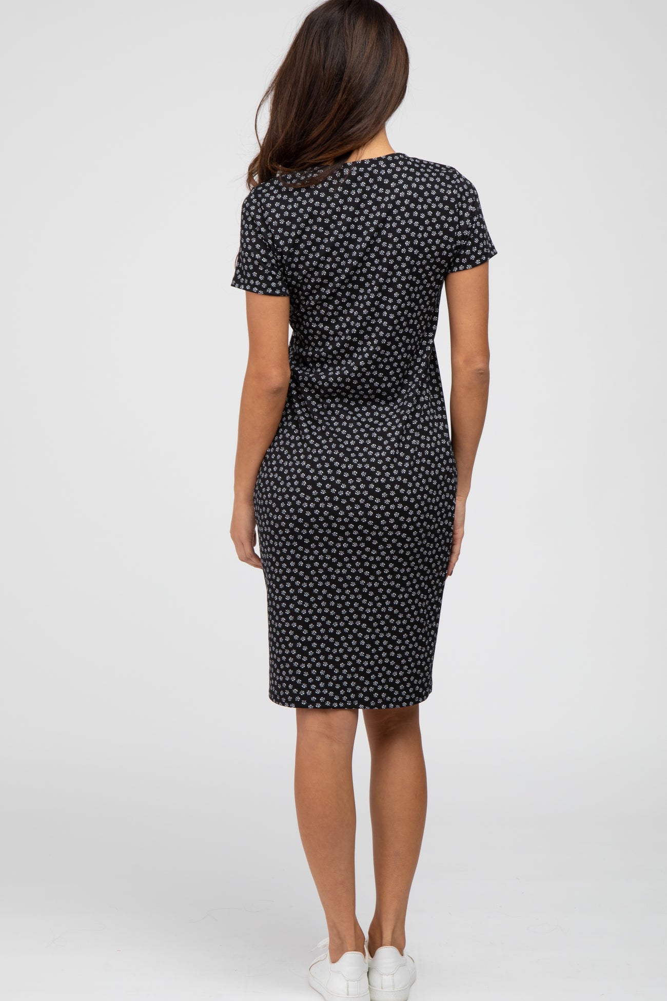 Back view of a woman wearing a black short sleeve knee-length dress with a white floral print and white sneakers