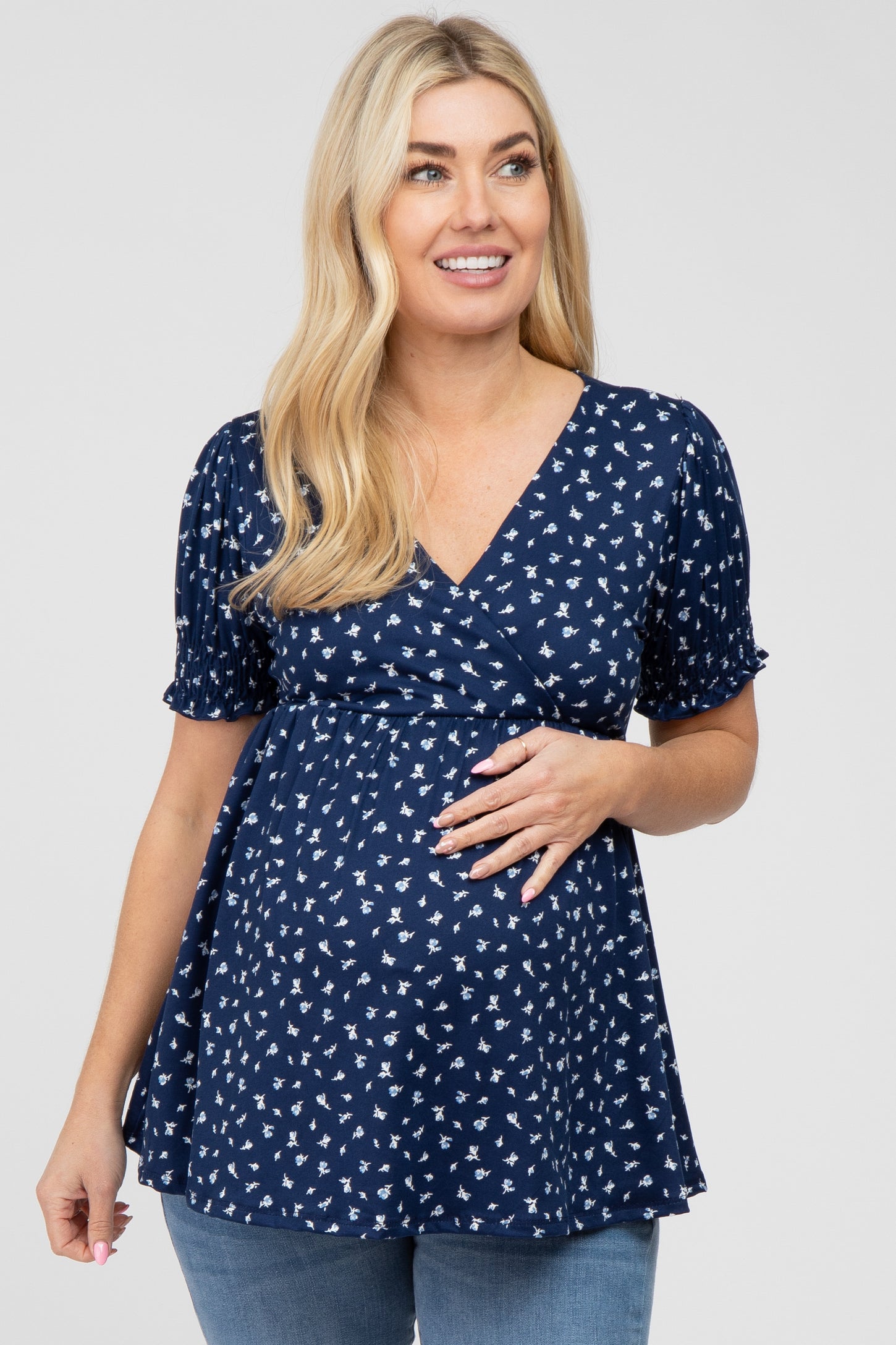 Pregnant woman wearing a navy blue floral maternity top with short puff sleeves and a wrap neckline
