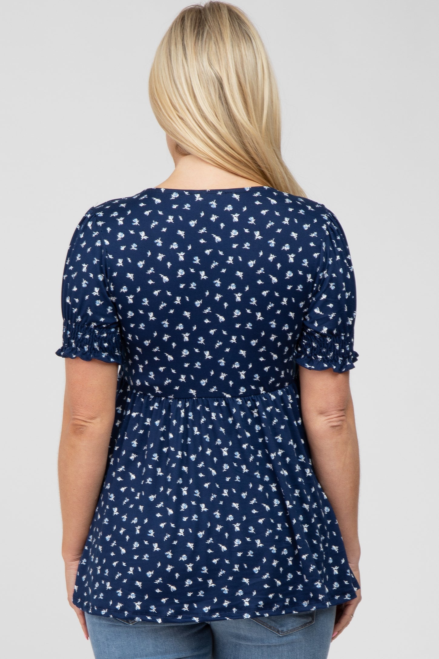 Back view of a woman wearing a navy blue floral print babydoll top with short ruffled sleeves