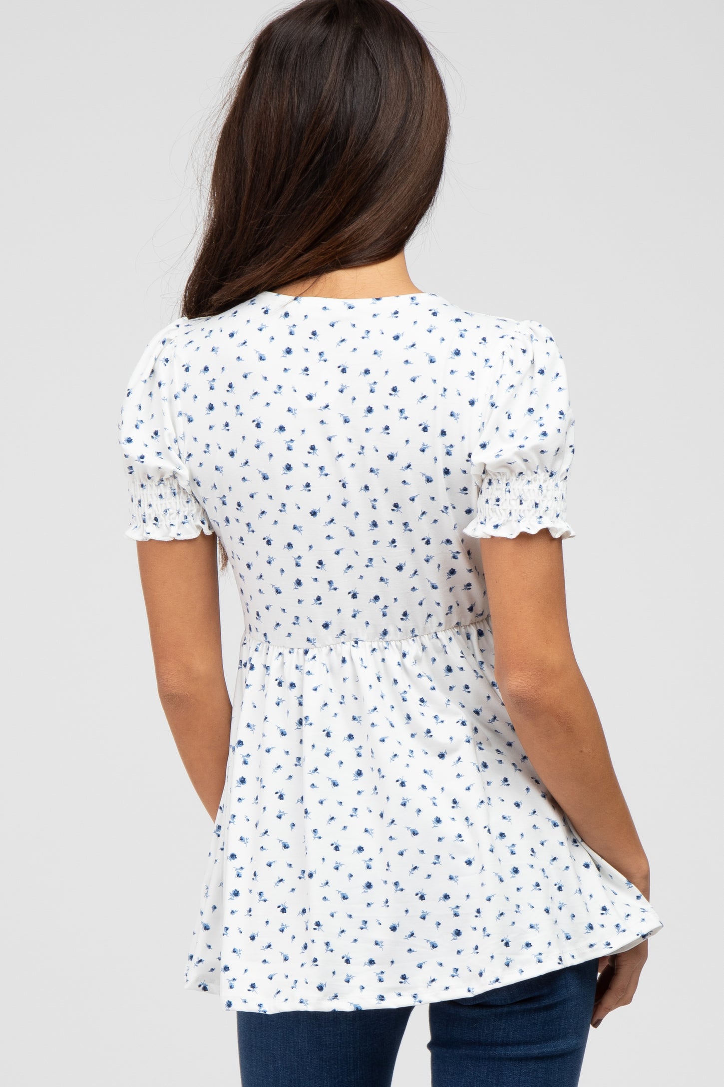 woman wearing a white short sleeve blouse with navy floral print and smocked details, shown from the back