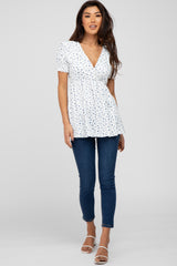 woman wearing a white short sleeve peplum top with blue floral print and paired with skinny jeans and heels
