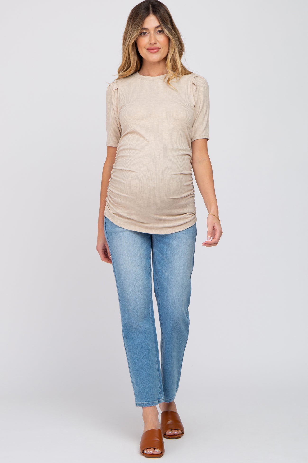 woman wearing a beige short sleeve maternity top with puff sleeves and a visible baby bump, paired with light blue jeans