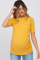 woman wearing a mustard yellow short sleeve maternity top with gathered sides and a visible baby bump