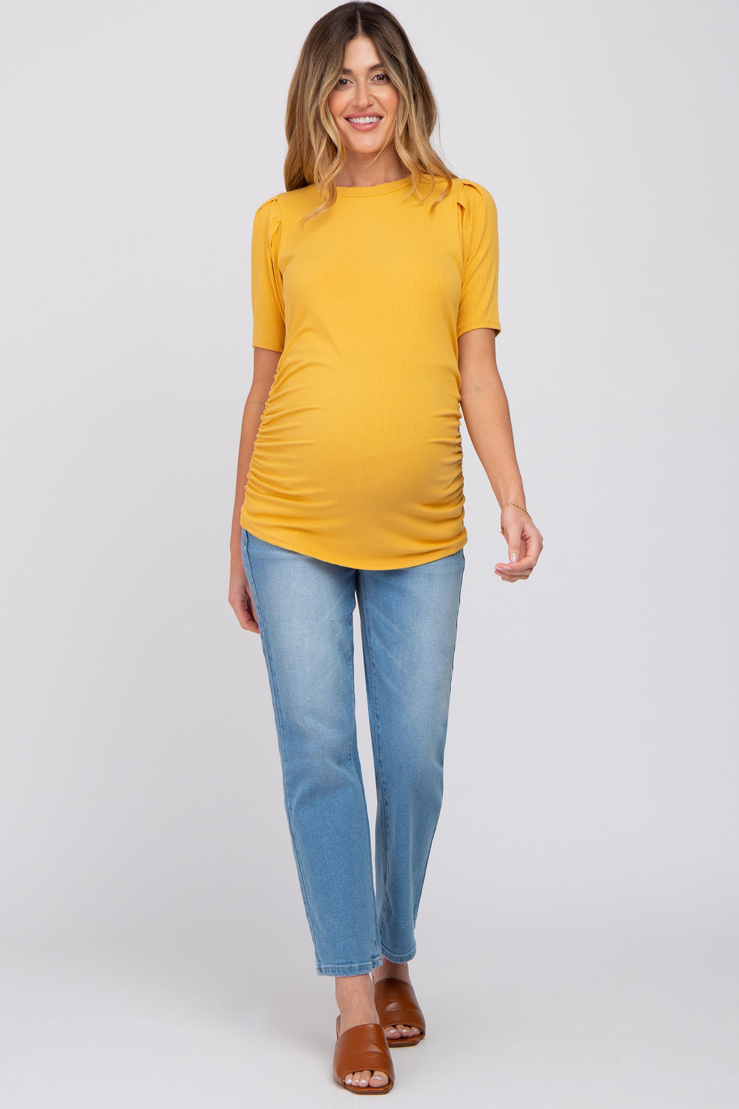 woman wearing a mustard yellow short sleeve maternity top and blue jeans, showcasing her baby bump