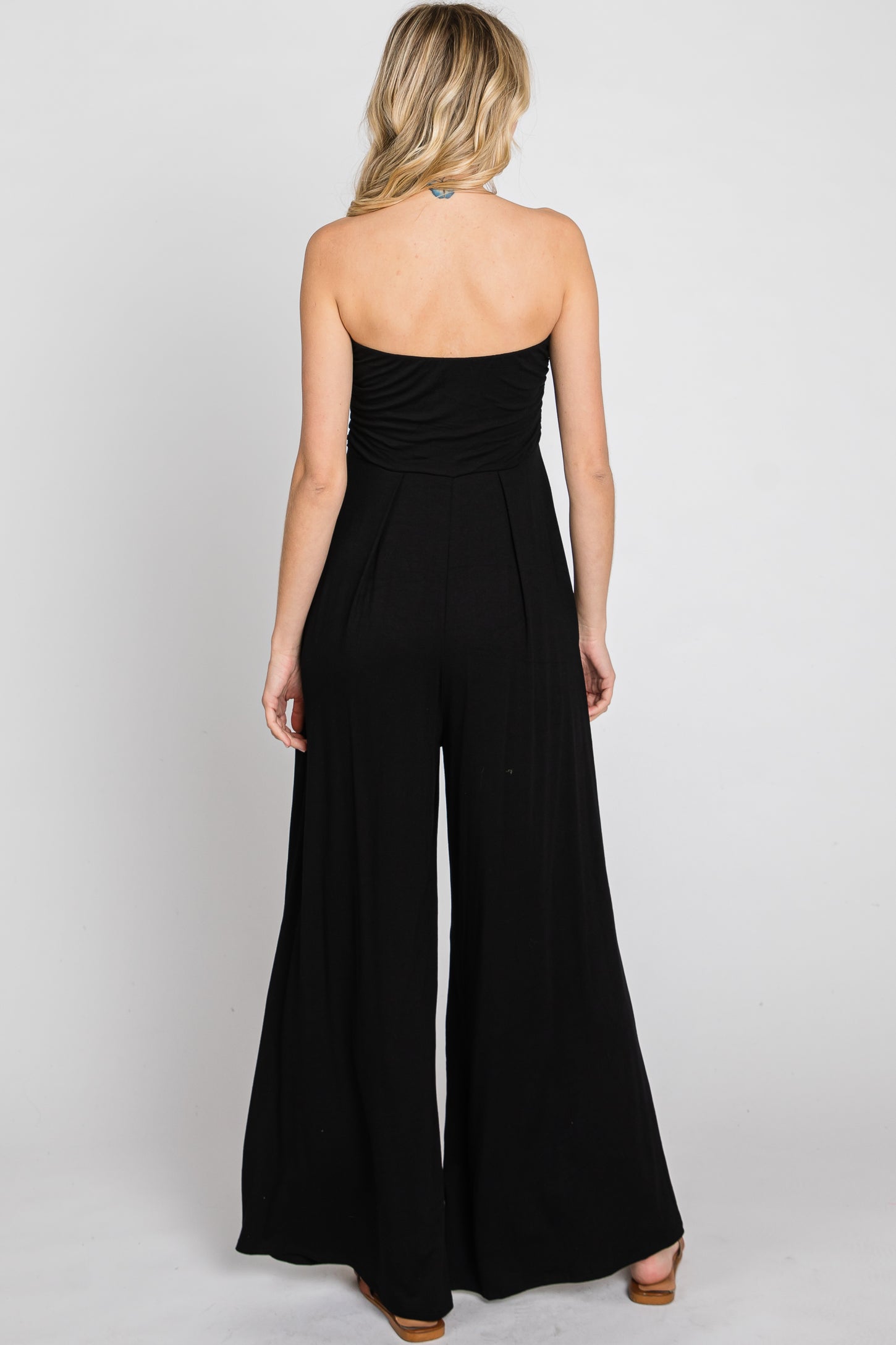 woman wearing a black strapless jumpsuit with a fitted bodice and wide-leg pants, viewed from the back