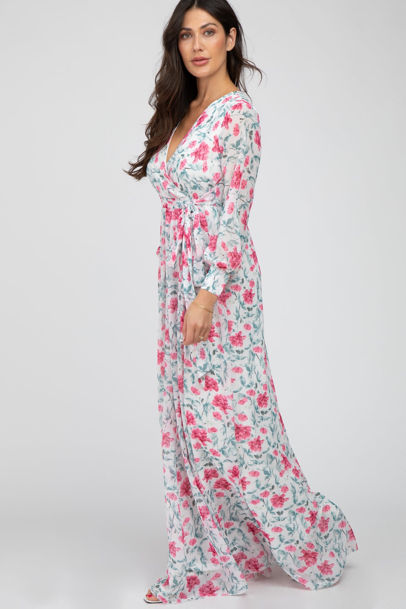 woman wearing a long sleeve white floral maxi dress with pink roses and a wrap v-neckline