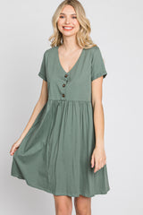 smiling woman wearing a short sleeve sage green v-neck babydoll dress with front buttons