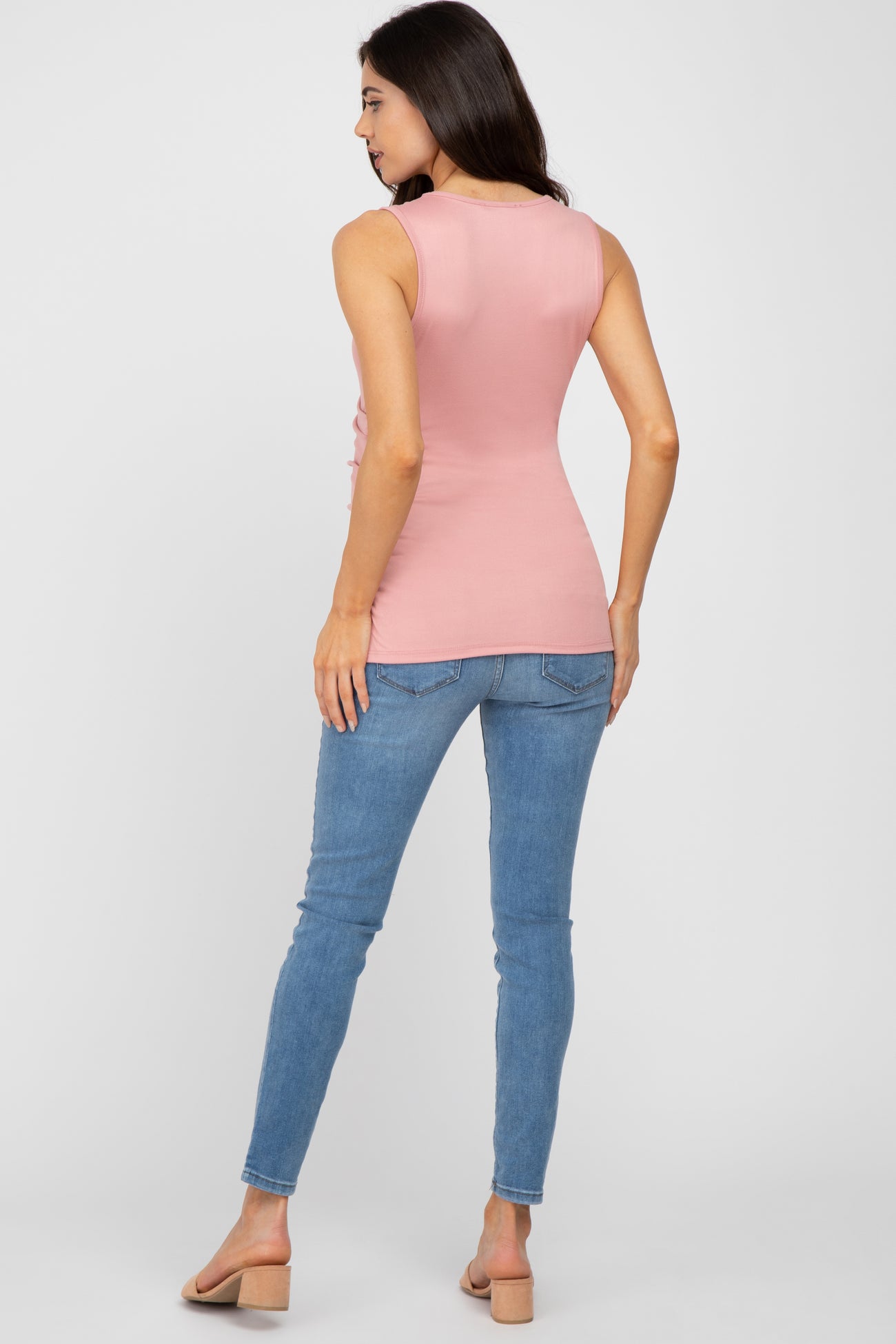 woman wearing a pink sleeveless maternity top with a fitted style and light blue skinny jeans