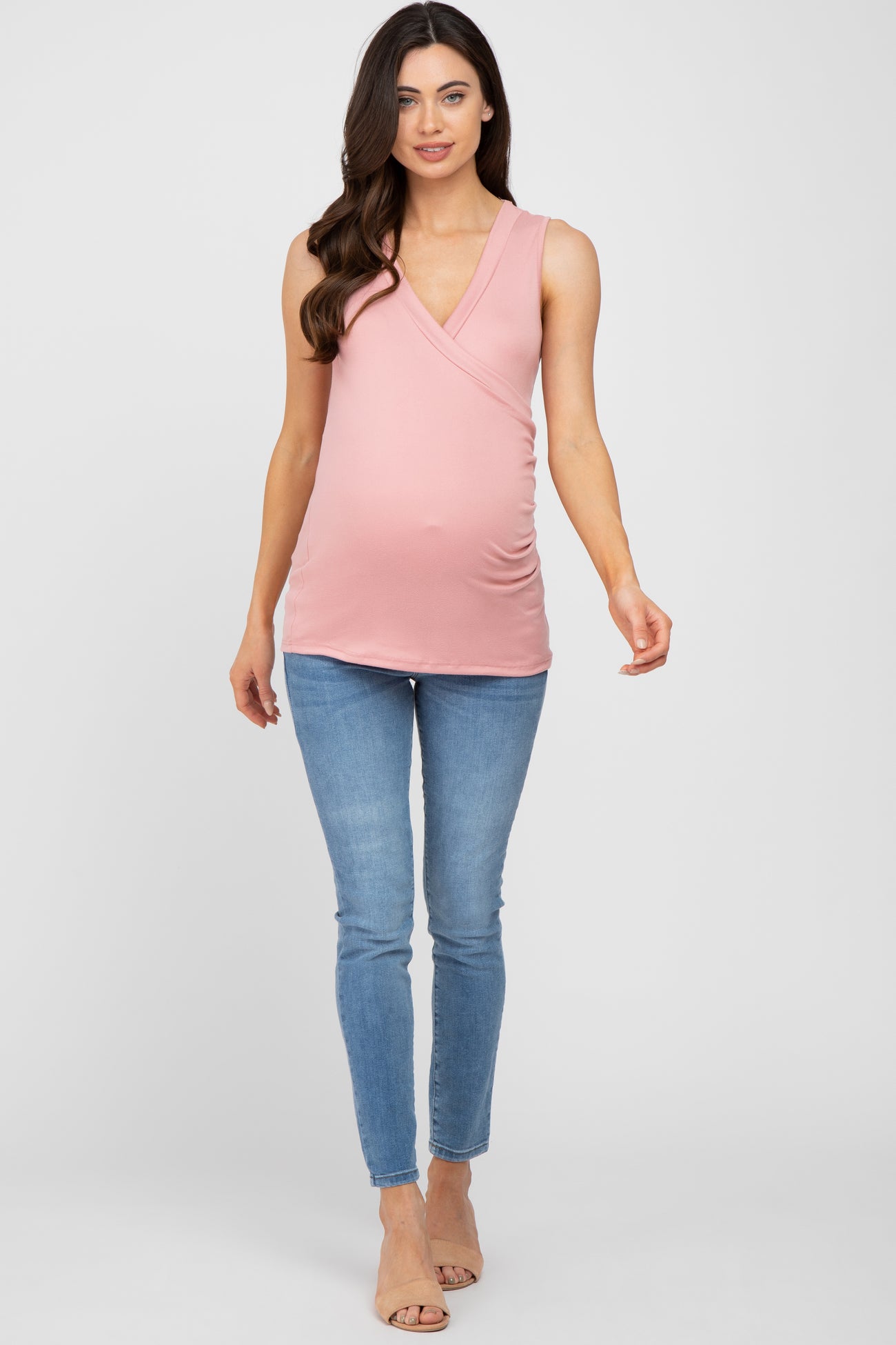 woman wearing a light pink maternity top with a wrap design and a baby bump, paired with skinny jeans