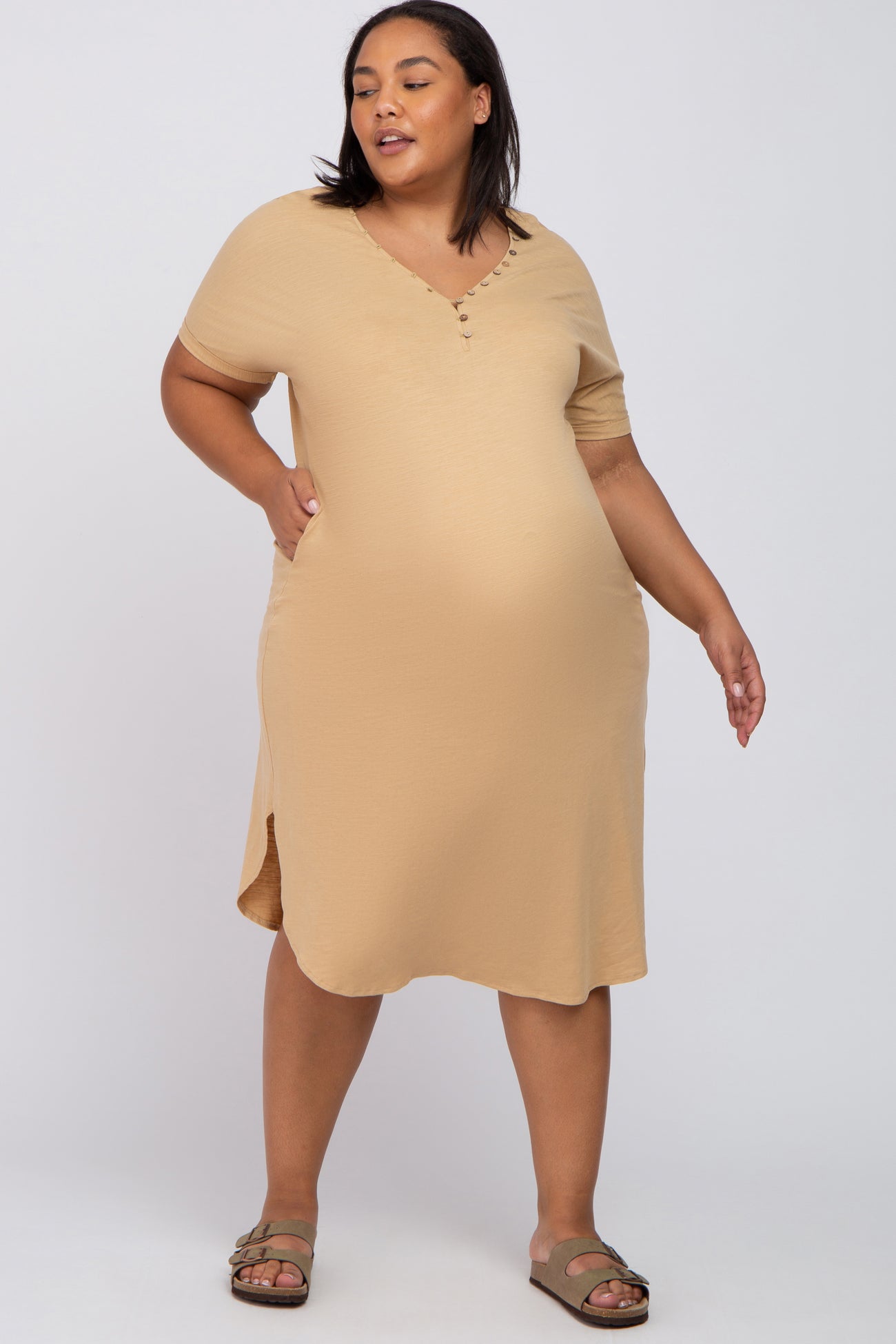 plus size woman wearing a tan short sleeve henley maternity dress and sandals